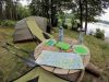 Campingplatz mit Zelt und massivem Holztisch. Auf dem Tisch liegen eine Karte und Campinggeschirr.