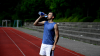 Arni steht in Sportkleidung auf einer Tartanbahn und trinkt aus einer Wasserflasche
