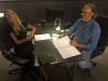 Paola und Luca sitzen am Tisch im Studio, sie lachen