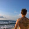 Tom steht am Strand, Rücken zur Kamera mit seinem Tatoo